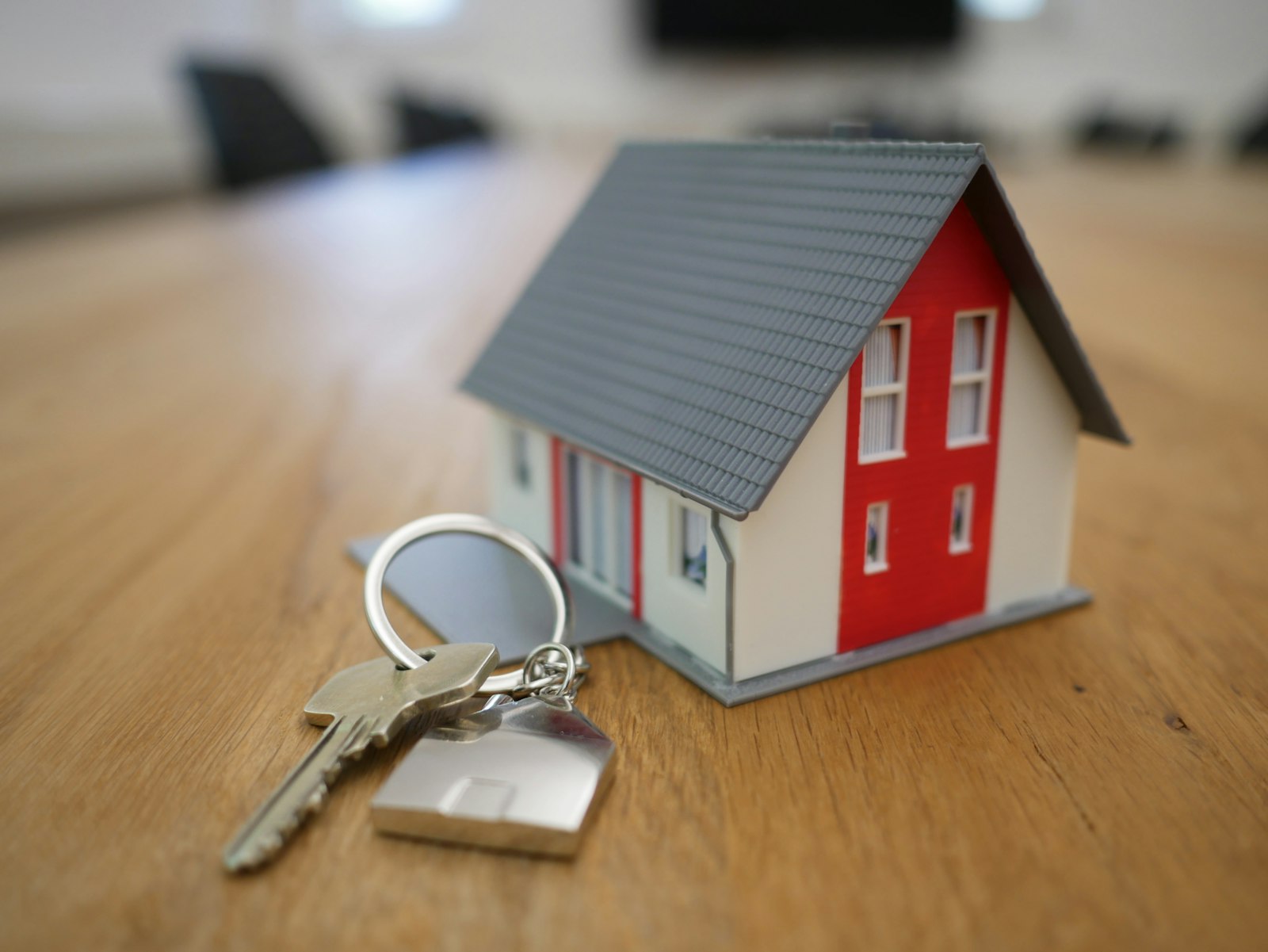 Small model house with a silver house key on a wooden table, representing buying and selling a home